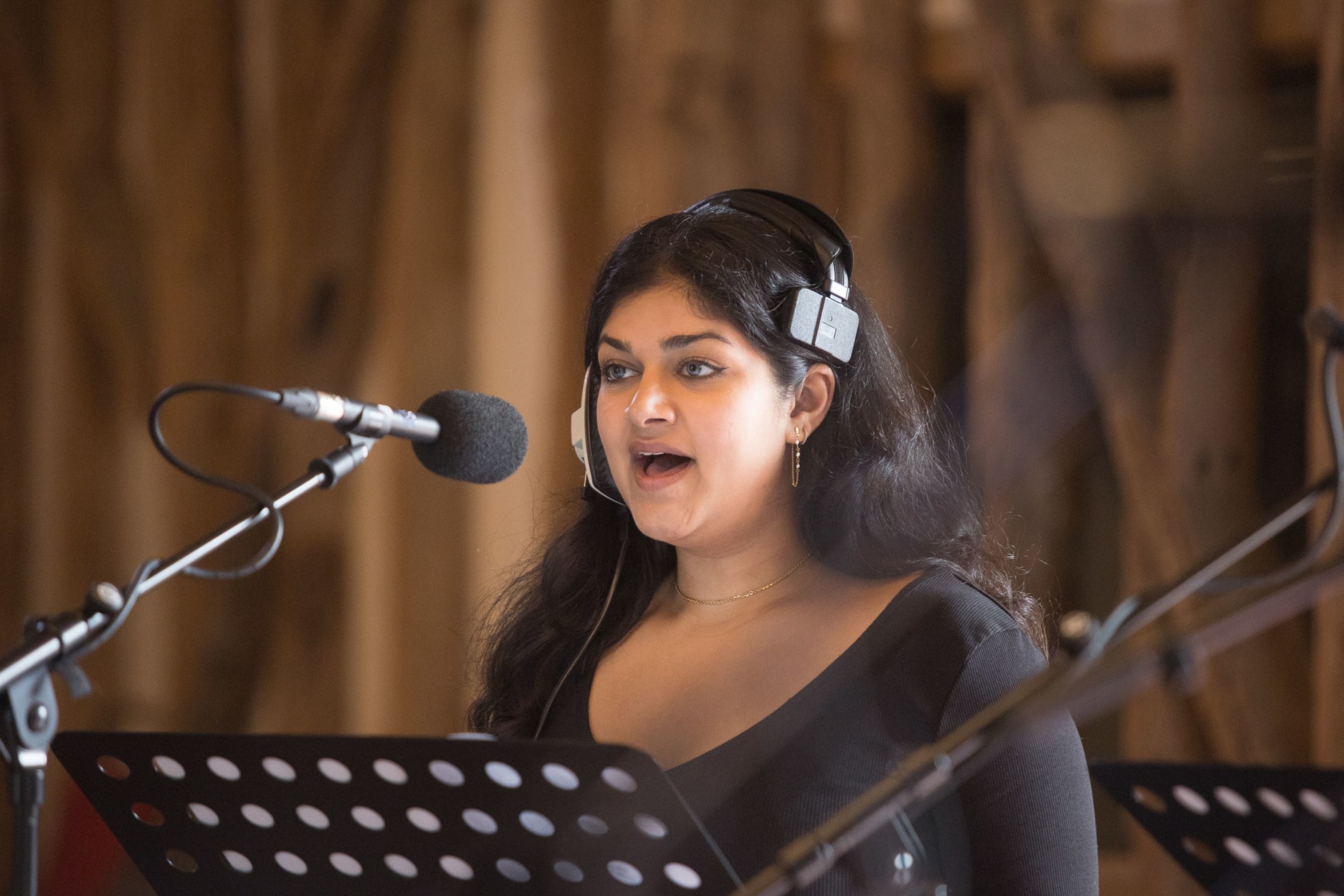 Action shot of Sarina, a south asian woman with long dark hair, singing in a recording studio with a headset
